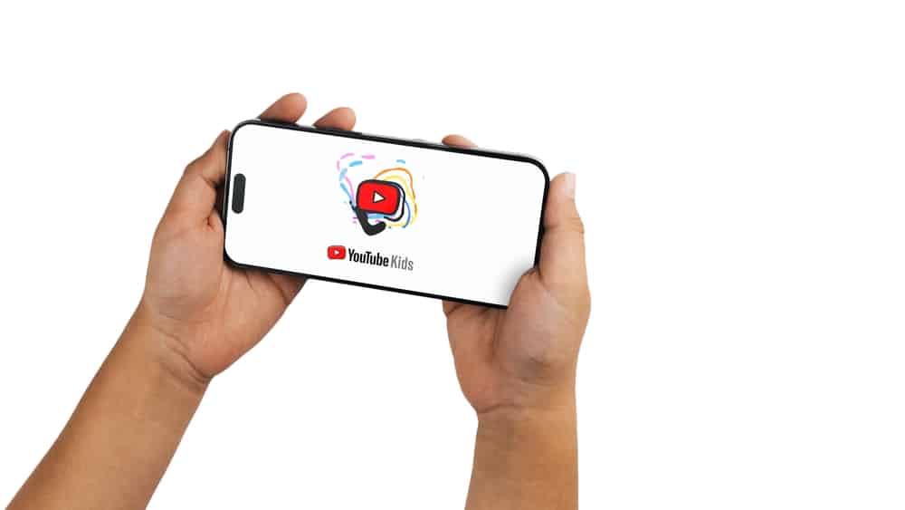 Child holding a smartphone iPhone 14 Pro with Youtube Kids app app on the screen. White background.