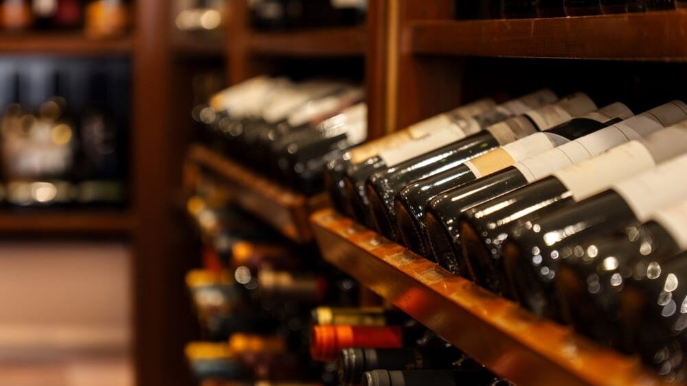 Bottles of black red wine lined up, stacked and resting diagonally on wooden shelves in a luxury collectible wine store.